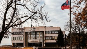A view of the Slovak Parliament building surrounded by autumn trees with the national flag waving under an overcast sky.