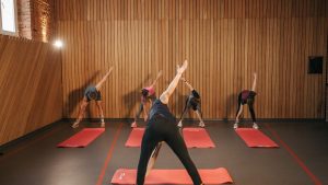 Yoga class with diverse adults stretching on mats in a cozy wooden studio.